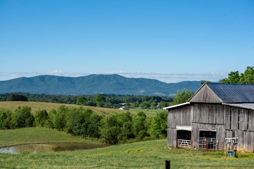 Scenic rural landscape featuring a rustic barn, lush green fields, and distant blue mountains under a clear sky.