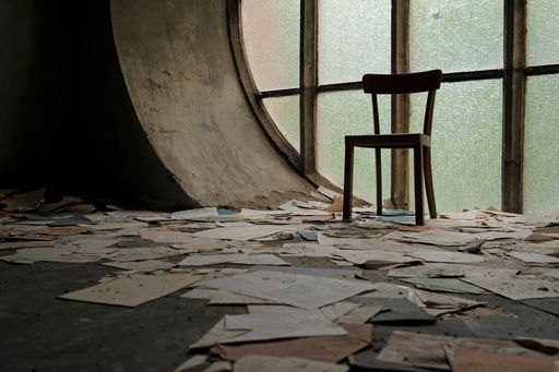 A closeup shot of a chair in front of a round window with papers and book pages lying on the ground