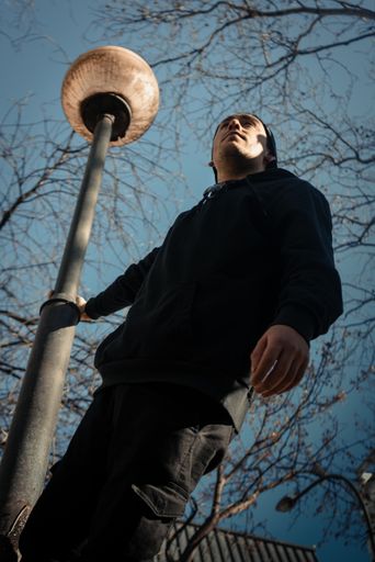 A low angle shot of a South American male in black clothing holding on from the lamp post