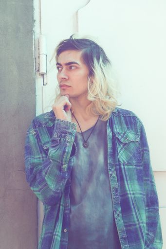 An attractive Armenian guy leaning on a white door while looking away from the camera