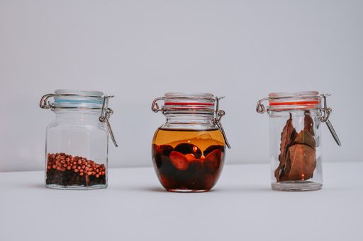 Three jars containing black and white pepper, olives and olive oil, bay leaves