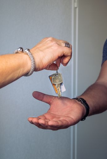 A vertical closeup shot of a landlord's hand presenting keys to a renter