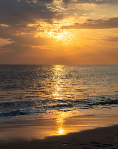 The golden sunset over a tranquil ocean with gentle waves and a sandy beach. Martha's Vineyard