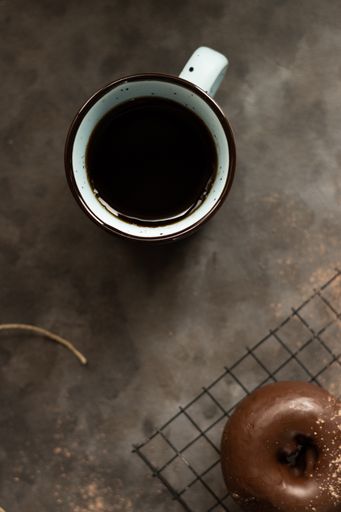 A vertical top view of a cup of coffee and a chocolate donut on a kitchen table