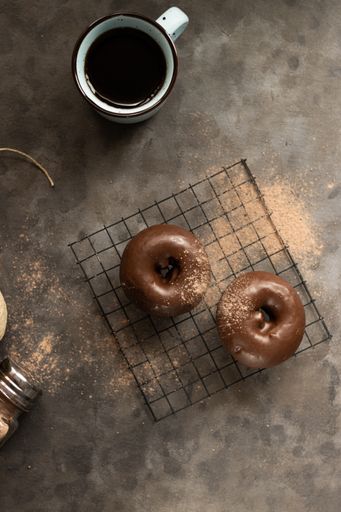 A vertical top view of a cup of coffee and chocolate donuts on a kitchen table with spilled cinnamon
