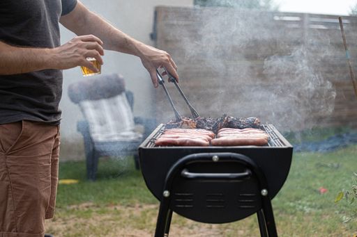 A man's hand cooking meat on a grill