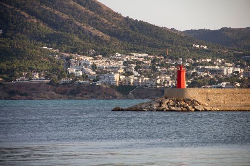 A scenic view of a red lighthouse on the coast against the City of Altea, Spain