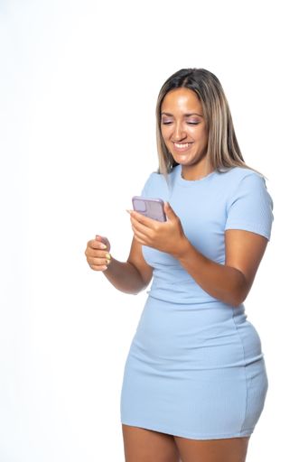 An isolated shot of a blonde Hispanic woman in blue dress happily communicating through her mobile phone