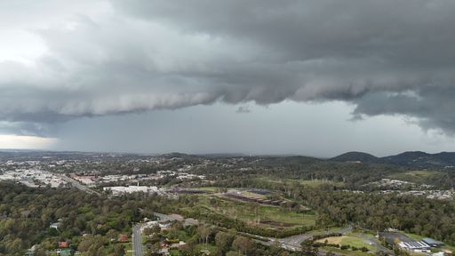Aerial view of a cityscape under dramatic storm clouds, showcasing urban and natural landscapes with a moody sky.