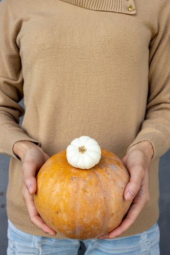 A woman holds an orange squash and a small white one. This is a summer harvest to decorate for the next season, autumn.