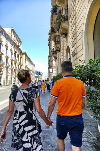 A vertical shot of a couple holding hands and walking in the street in Catania, Italy