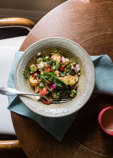 A top view shot of an Italian salad with fresh tomatoes, basil, mozzarella, panzanella, and a cup of coffee