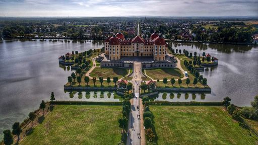 Aerial view of Moritzburg Castle surrounded by serene lakes and lush greenery in Saxony, Germany, on a sunny day.