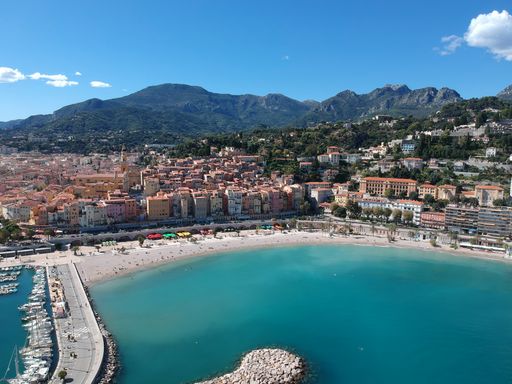 An aerial view of a beach with a port and dense buildings under a clear sky in Menton, French Riviera