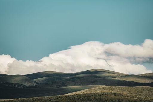 Rolling hills under a bright blue sky with fluffy white clouds creating a serene landscape.