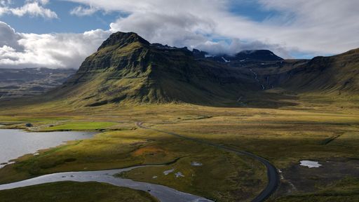 A breathtaking aerial view of a mountain landscape with a winding road and cloudy sky in Iceland.