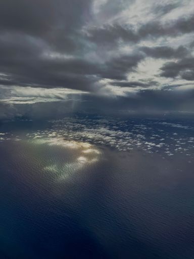 Aerial view of ocean waves reflecting sunlight under a dramatic cloudy sky