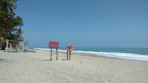 The beach with a caution sign on it surrounded by greenery and the sea under the sunlight