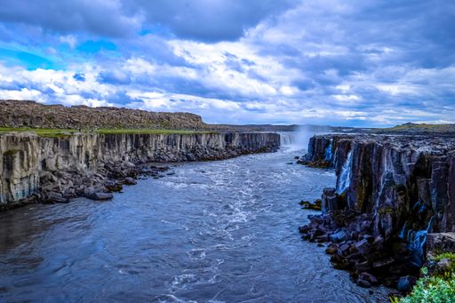 A beautiful shot of water in the middle of two rocky cliffs under a cloudy sky with a waterfall in the distance