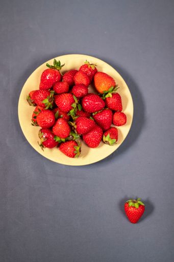 A top view of fresh strawberries in a wooden bowl on a gray background