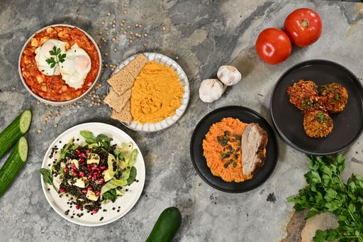 Top view of a variety of Mediterranean dishes including shakshuka, hummus with crackers, and a lentil salad on a stone table.