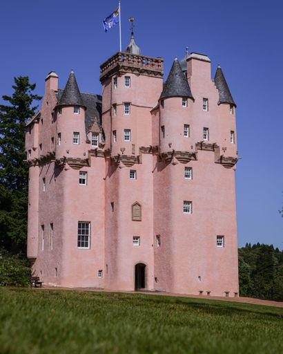 Craigievar Castle, a pink-hued historic castle in Scotland, under a clear blue sky, surrounded by lush greenery.