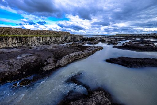 A beautiful shot of water flowing in the middle of rocks and cliffs in the distance under a cloudy sky