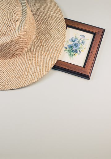 A vertical shot of a straw hat and blue flowers painting with a wooden frame, on a white surface