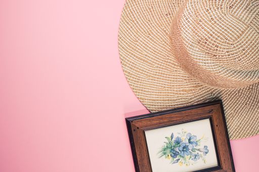 A top view of a framed picture of flowers with a sun hat on a pink surface
