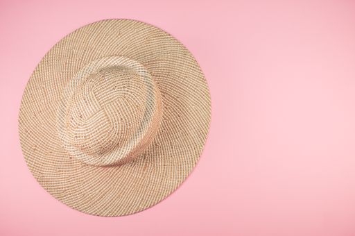 A top view of a sun hat on a pink surface with space for text