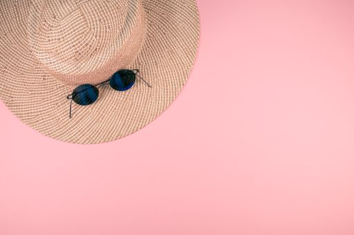 A top view of a straw hat and sunglasses on a pink surface