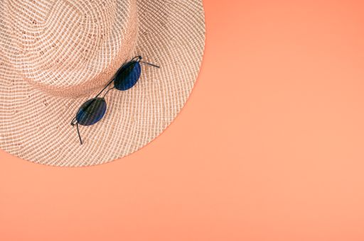 A top view of a sun hat with a pair of sunglasses on it on an orange surface with space for text