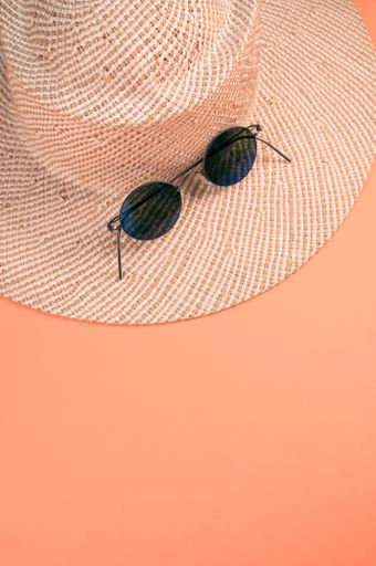 A vertical shot of a straw hat and sunglasses on an orange surface