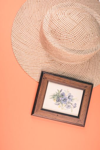 A vertical shot of a straw hat and blue flowers painting with a wooden frame, on an orange surface