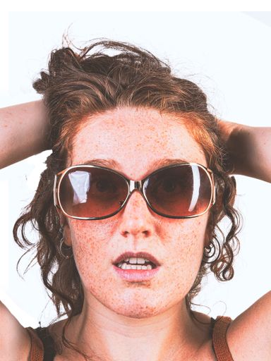 A vertical shot of a young sexy female with sunglasses posing on a white background