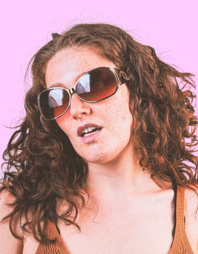 A vertical shot of a young sexy female with sunglasses posing on a pink background