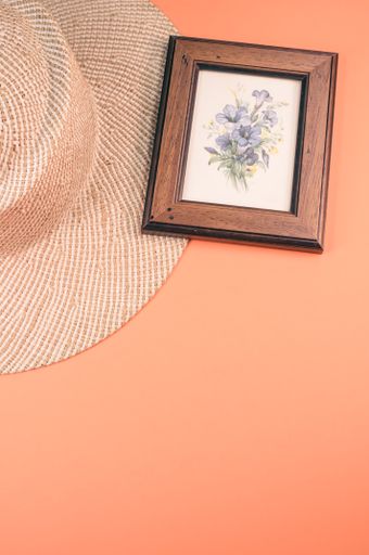 A vertical shot of a straw hat and blue flowers painting with a wooden frame, on an orange surface