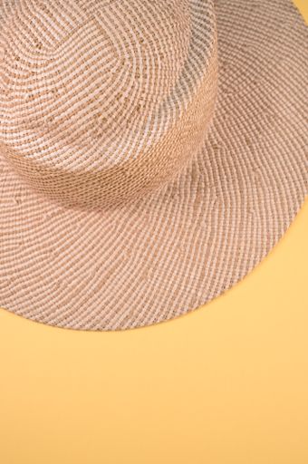 A vertical shot of a sun hat on a yellow surface with space for text