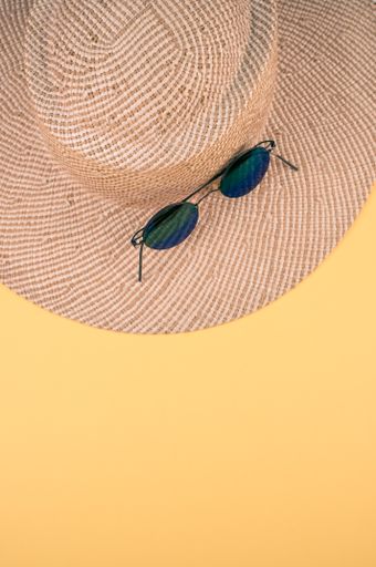 A vertical shot of a straw hat and sunglasses on a yellow surface