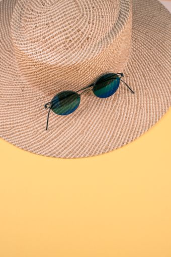 A vertical shot of a sun hat with a pair of sunglasses on it on a yellow surface with space for text