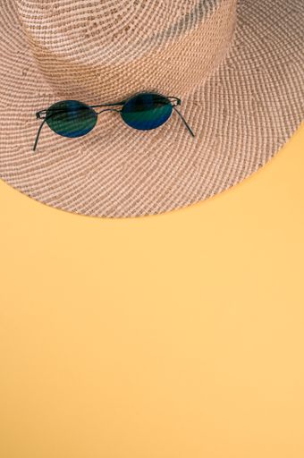 A vertical shot of a straw hat and sunglasses on a yellow surface