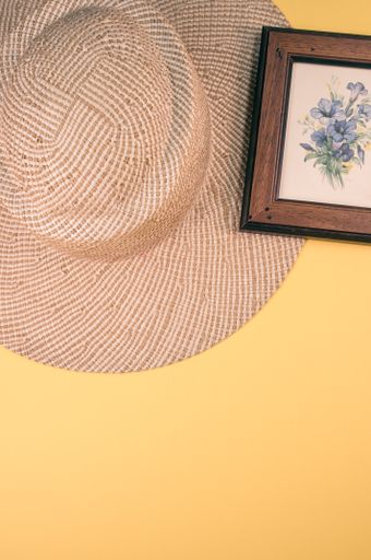 A vertical shot of a straw hat and blue flowers painting with a wooden frame, on a yellow surface