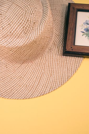 A vertical shot of a straw hat and blue flowers painting with a wooden frame, on a yellow surface