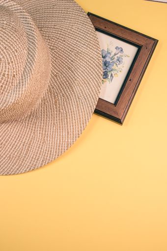 A vertical s a framed picture of flowers with a sun hat on a yellow surface