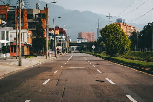 A road surrounded by greenery and buildings with mountains under the sunlight on the background