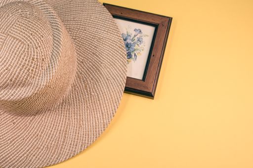 A top view of a framed picture of flowers with a sun hat on a yellow surface
