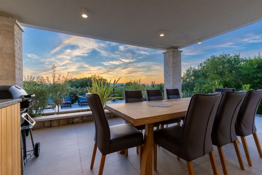 Outdoor dining area with modern furniture overlooking a lush garden and sunset sky.