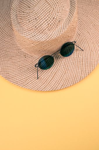 A vertical shot of a straw hat and sunglasses on a yellow surface