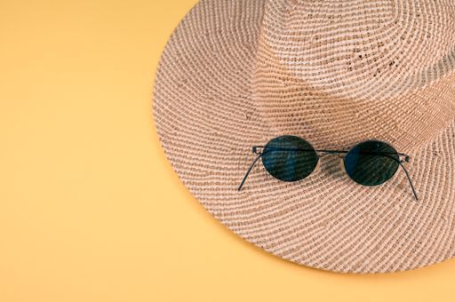 A top view of a straw hat and sunglasses on a yellow surface