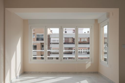 An empty apartment room with beige walls and sunlight coming from the windows